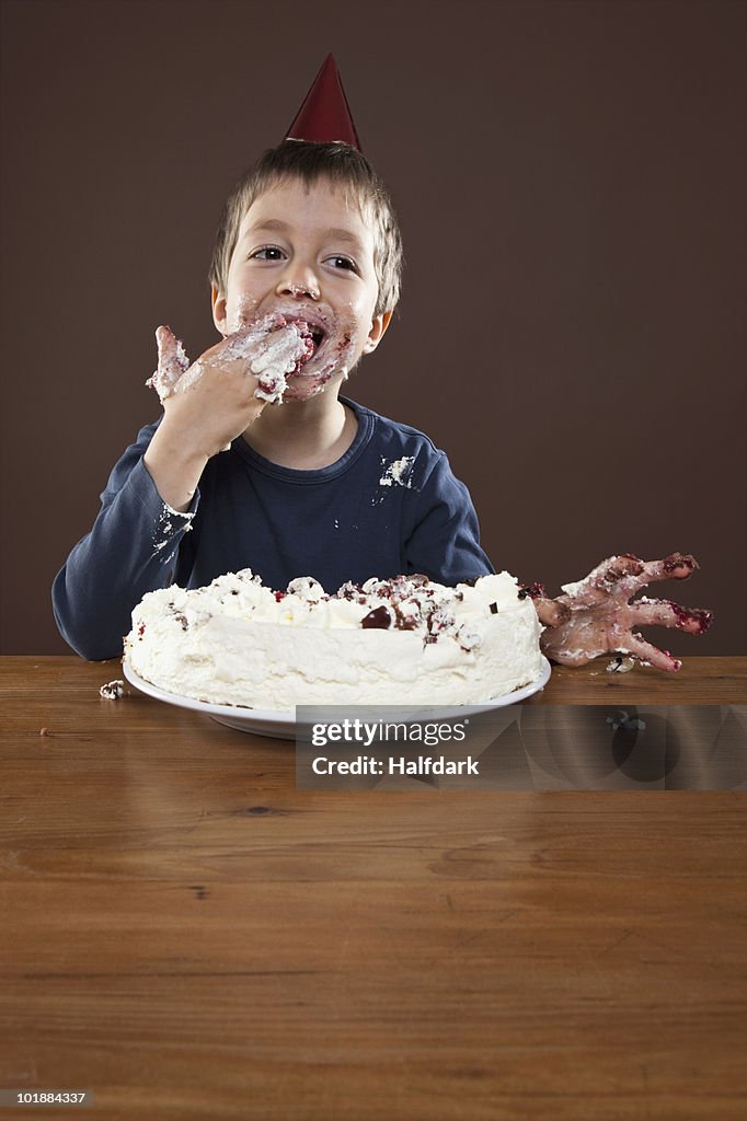 A boy wearing a party hat eating pie with his hands, studio shot
