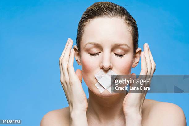 a woman with tape covering her mouth, gesturing in frustration - schweigen stock-fotos und bilder