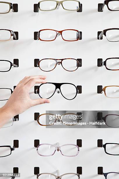 a human hand choosing a pair of glasses in an eyewear store - pair stock photos et images de collection