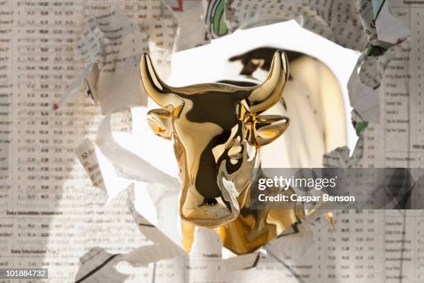 A golden bull breaking through the finance section of a newspaper