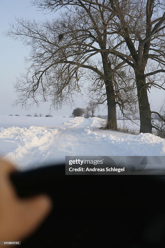 View of snow covered country road through car windshield