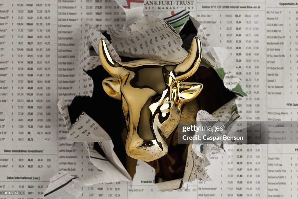 Detail of a golden bull breaking through the finance section of a newspaper