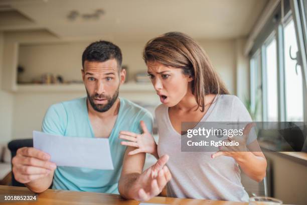 shocked young couple looking at their bills at home - shock stock pictures, royalty-free photos & images