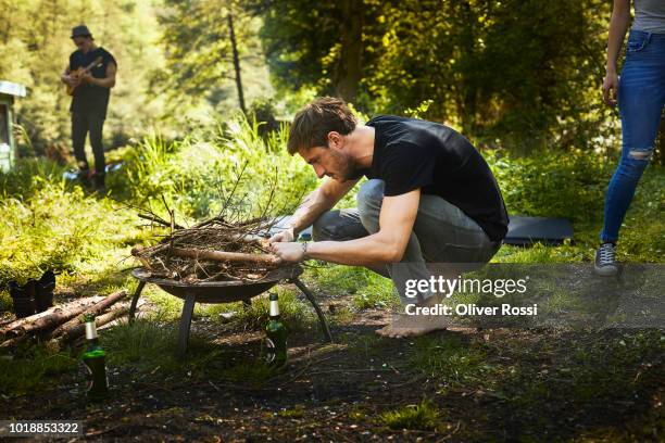 man preparing a campfire in a brazier - brasero photos et images de collection