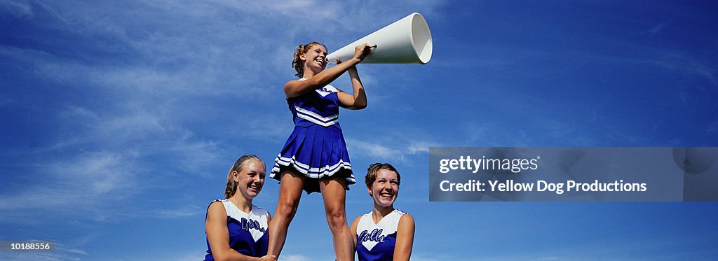 Two cheerleaders supporting third cheerleader with megaphone