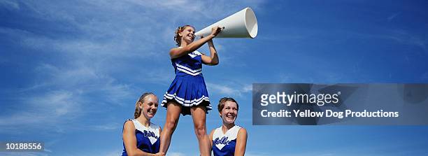 two cheerleaders supporting third cheerleader with megaphone - cheerleader imagens e fotografias de stock