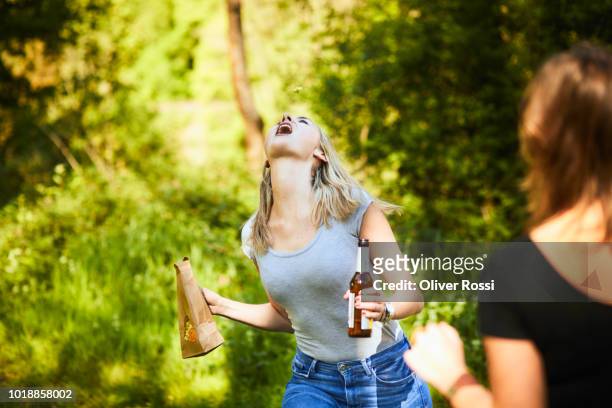 woman holding beer bottle trying to catch popcorn with her mouth - beer bottle mouth stock-fotos und bilder