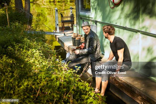 young man with guitar and friend sitting on a houseboat - houseboat stock pictures, royalty-free photos & images