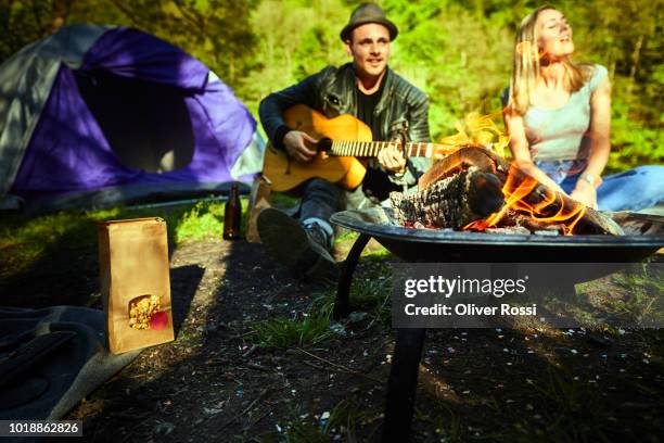 young couple sitting at the fire playing guitar - brazier stock pictures, royalty-free photos & images