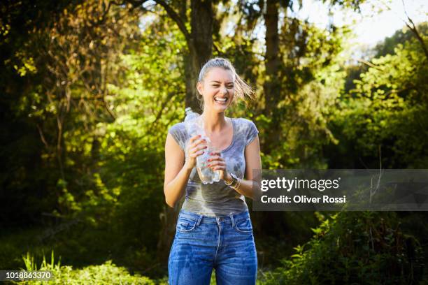 laughing young woman with wet clothes holding bottle of water - women in wet tee shirts stock pictures, royalty-free photos & images