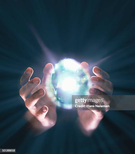 hands coming around bright ball of light - magia foto e immagini stock