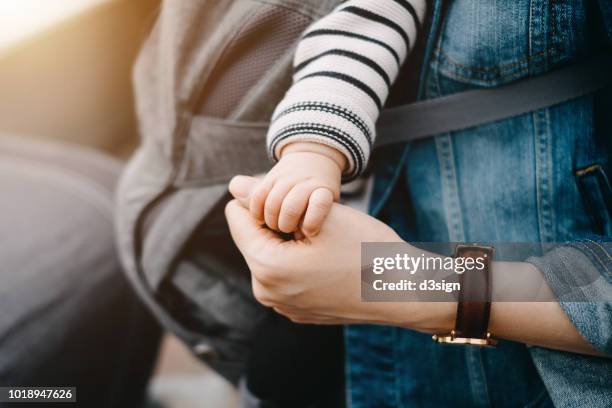 close up of mother carrying baby and holding hand - baby carrier stock pictures, royalty-free photos & images