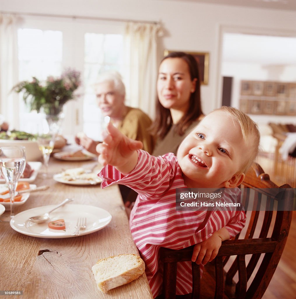 Female generational family at dinner table, girl (2-4 years) reaching