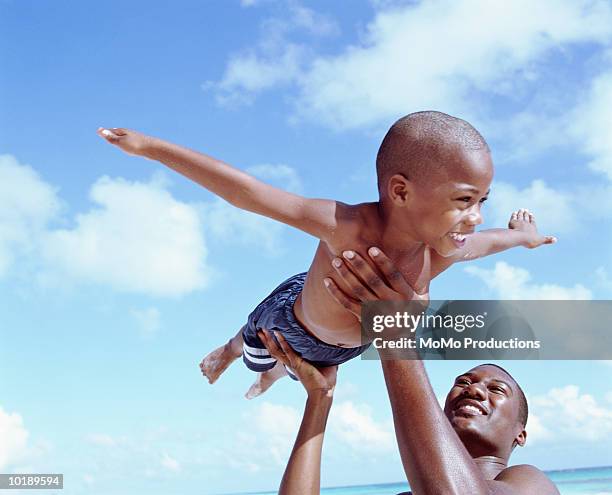 father lifting son (6-8 years) in air at beach, son pretending to fly - flying dad son stock pictures, royalty-free photos & images