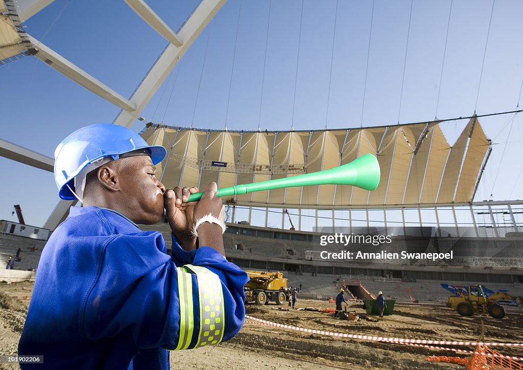 Construction worker blowing vuvumzela in front of construction work, Moses Mabhida Stadium, Durban, KwaZului-Natal Province, South Africa