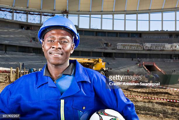 construction worker with football in front of construction work, moses mabhida stadium, durban, kwazului-natal province, south africa - football helmet foto e immagini stock