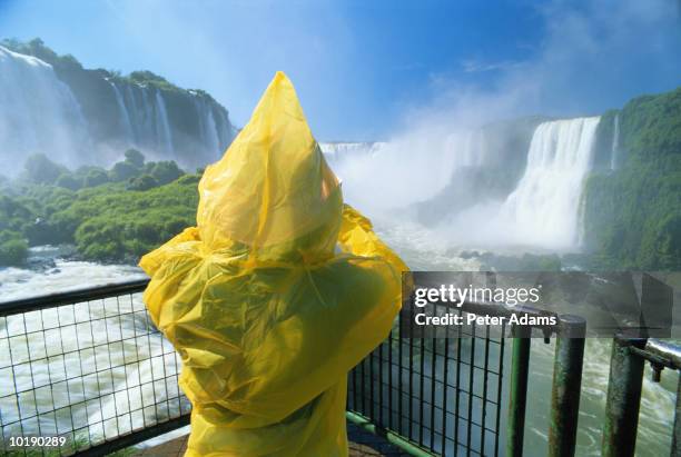 brazil, iguacu falls, person in waterproof jacket, rear view - iguacu falls stock pictures, royalty-free photos & images