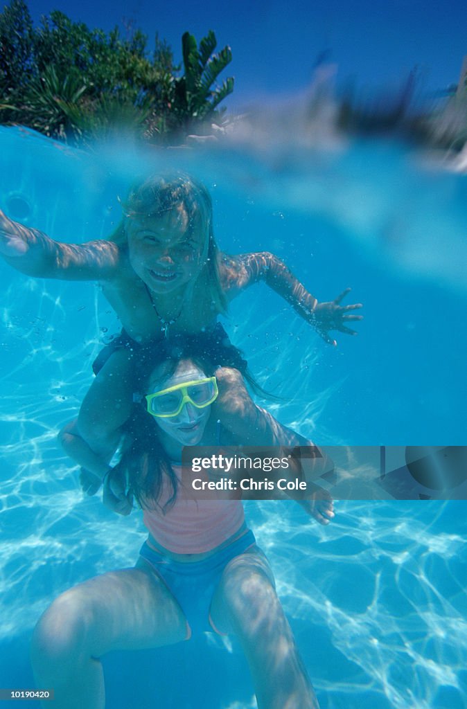 Two girls in pool, underwater view, portrait