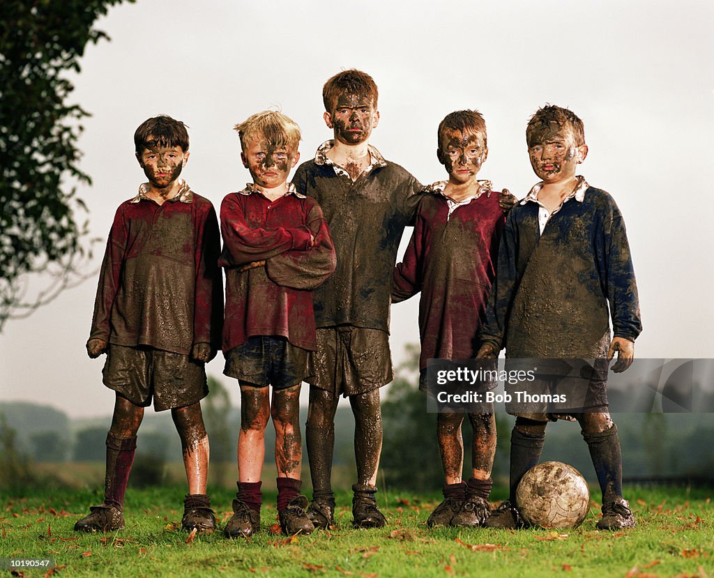 Five boys (8-10) with football, covered in mud, portrait