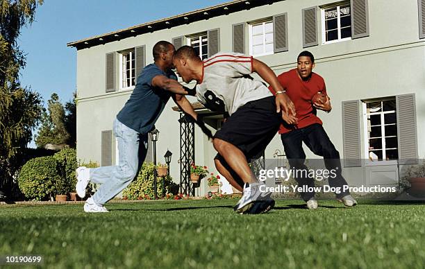 three men playing football outside house - tackle american football positie stockfoto's en -beelden