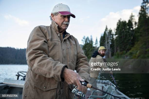 Senior Man with Adult Grandson Fishing on a Mountain Lake with Their Boat