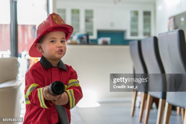 kleiner junge vorgibt, ein feuerwehrmann zu sein - feuerwehrhelm stock-fotos und bilder