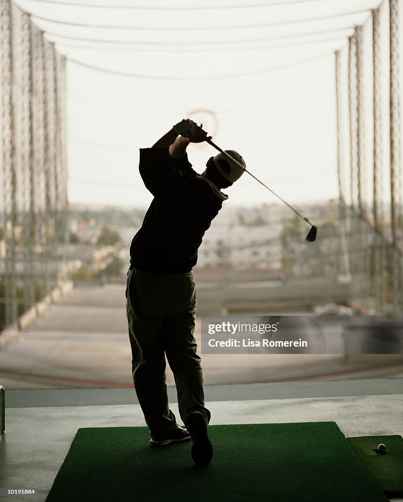 Man practicing golf swing in driving range, rear view