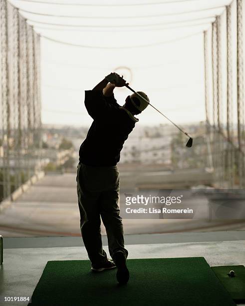 man practicing golf swing in driving range, rear view - drivingrange stockfoto's en -beelden