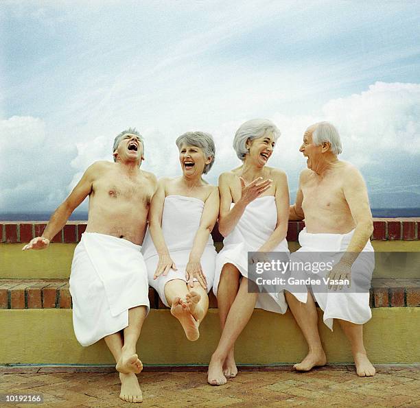 two mature couples sitting on wall wearing towels, laughing - enrolado em toalha de banho - fotografias e filmes do acervo