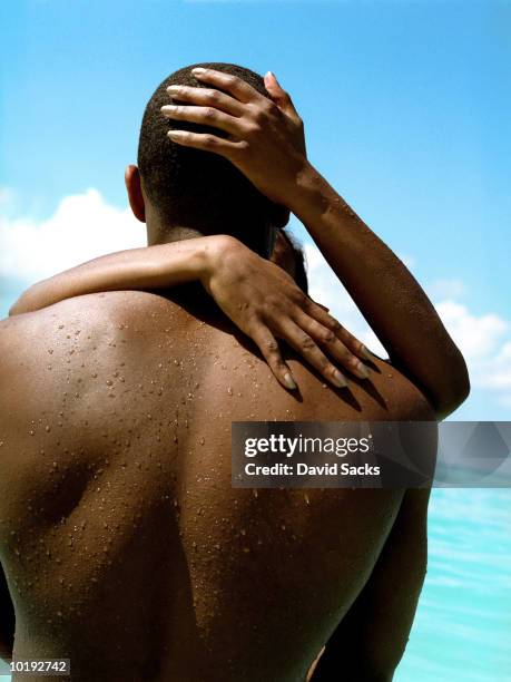 young couple embracing in sea, close-up, rear view - african american women wet stock-fotos und bilder