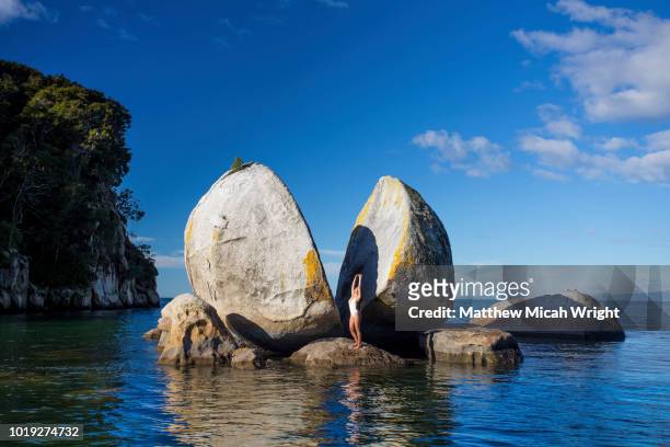a woman in a bikini poses in front of one of new zealand's famous landmarks; able tasman national park's split apple rock. - nelson imagens e fotografias de stock