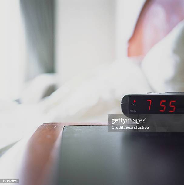 digital alarm clock by bed in hotel room (focus on clock) - orologio sveglia foto e immagini stock