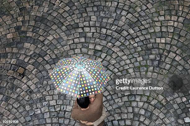 couple embracing under umbrella in cobbled street, elevated view - sharing umbrella stock pictures, royalty-free photos & images