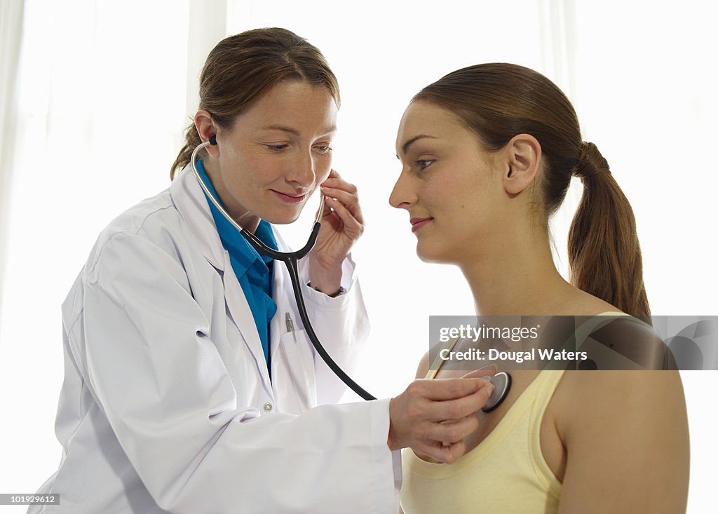 Female doctor using stethoscope on patient.