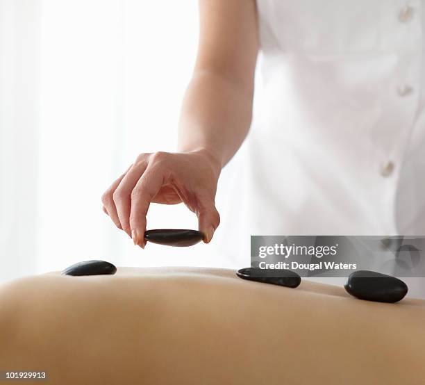 therapist placing hot stones on womans back. - lastone terapi bildbanksfoton och bilder