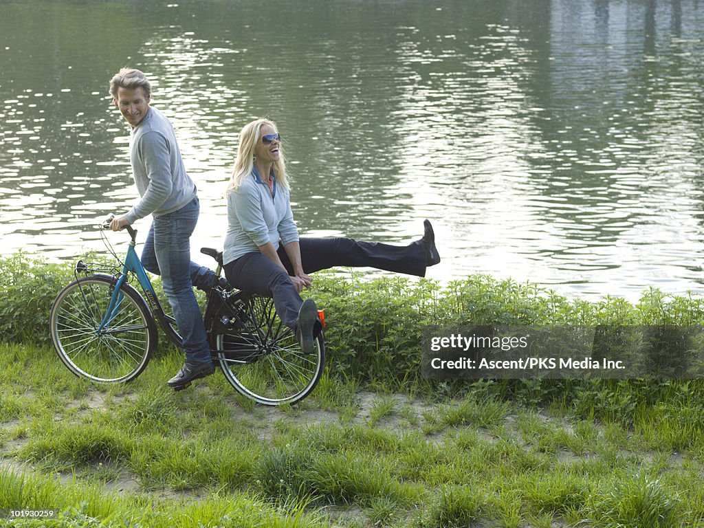 Couple double on bicycle next to river