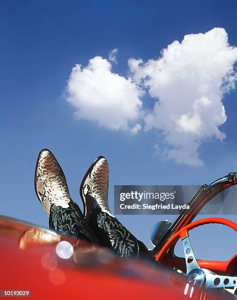 man wearing cowboy boots resting feet over side of sports car, close-u - cowboy boots stock pictures, royalty-free photos & images