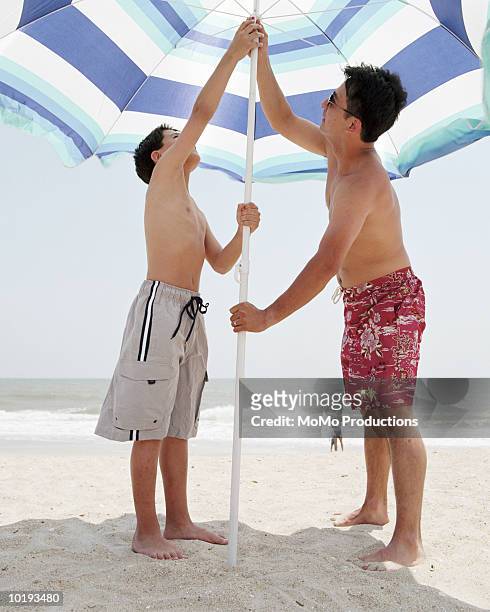 father and son (10-12) opening beach umbrella - open day 13 stock pictures, royalty-free photos & images