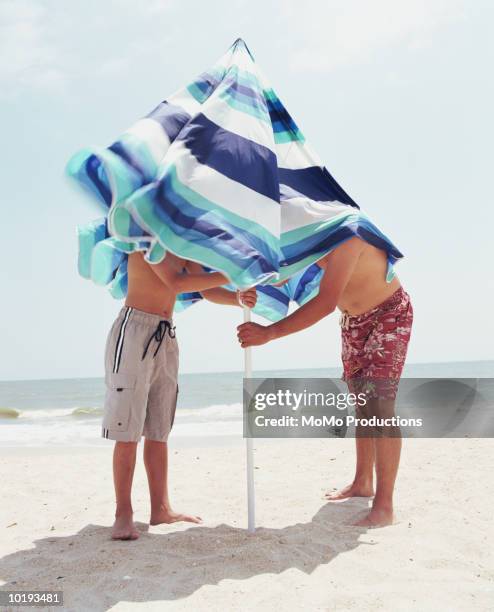 father and son securing beach umbrella - parasols stockfoto's en -beelden