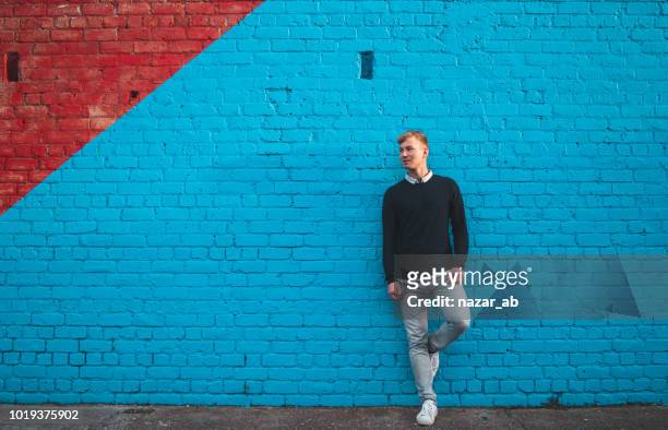 ung man står framför stora teal blue wall. - modern manlighet bildbanksfoton och bilder