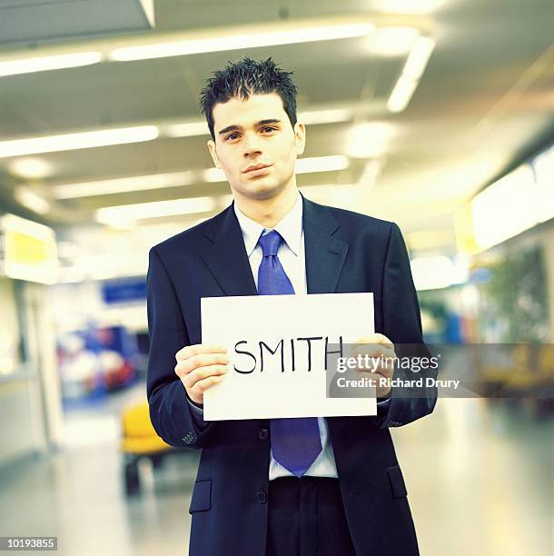 businessman holding 'smith' name card in airport, portrait - departure board front on fotografías e imágenes de stock