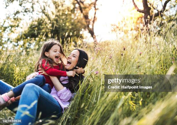 happy mother and her small daughter lying down on the grass in spring nature, laughing. - white flower field foto e immagini stock