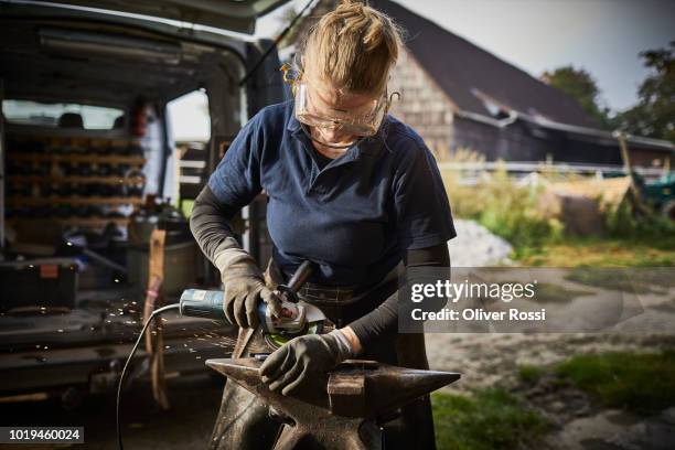 female farrier working with grinder on anvil - blacksmith sparks stock-fotos und bilder