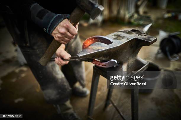 close-up of farrier forging horseshoe on anvil - smeden stockfoto's en -beelden