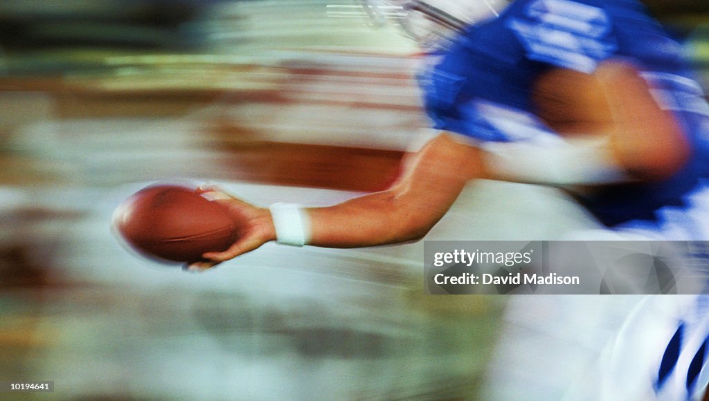 Male quarterback handing off football, mid section (long exposure)