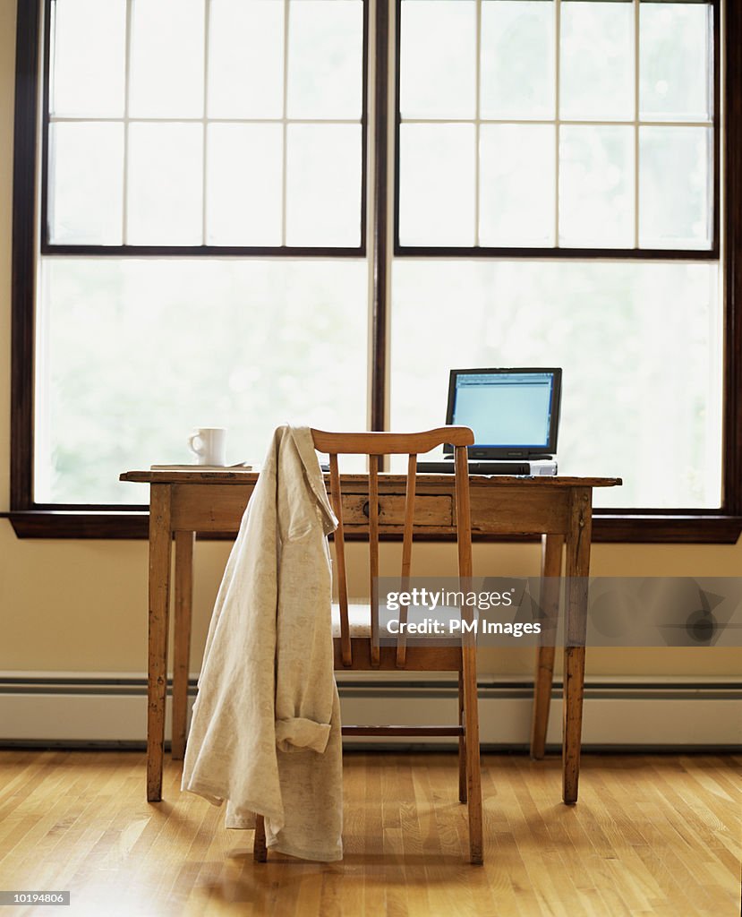 Shirt on chair and laptop sitting on desk by window