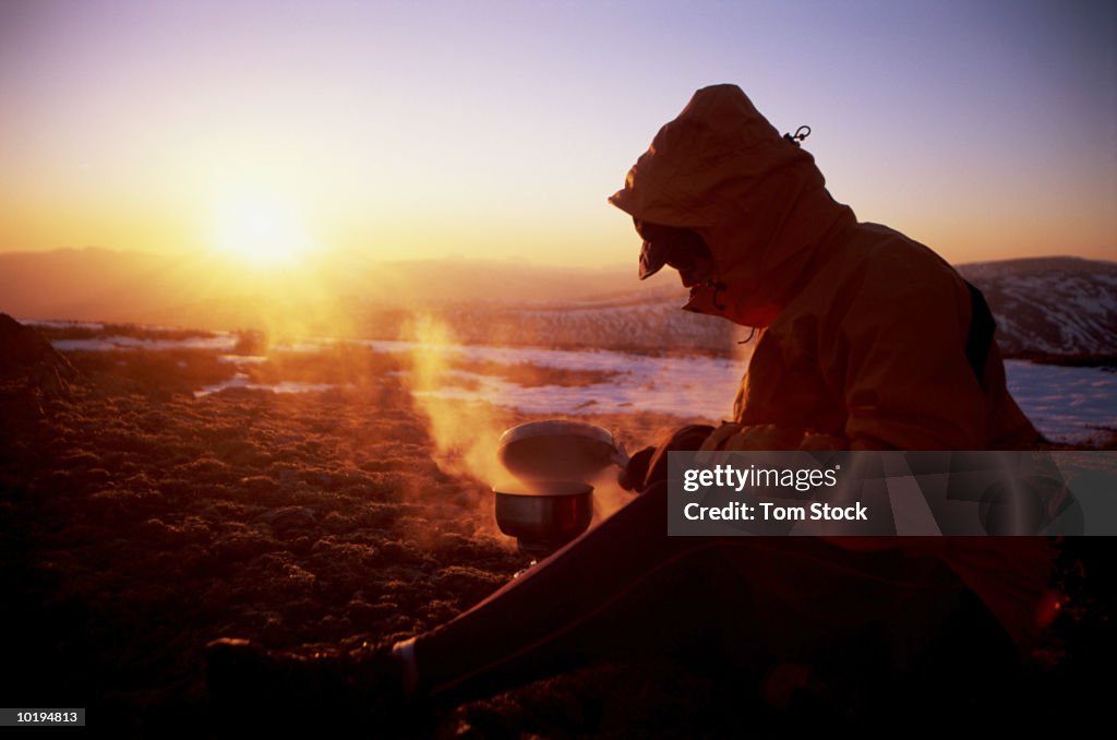 England, Cumbria, Lake District, Ullswater, female hiker cooking at su