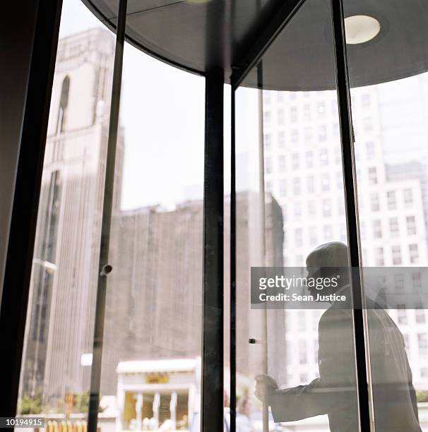 businessman pushing through revolving doors - revolving door stock pictures, royalty-free photos & images