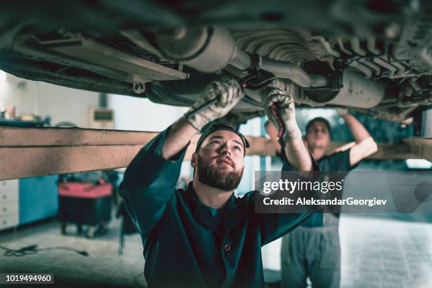 team of mechanics repairing car exhaust system - spoil system stock pictures, royalty-free photos & images