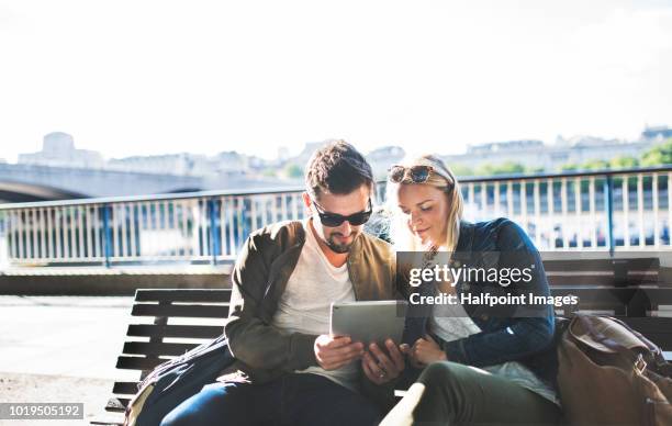 a young couple sitting on a bench on the city street, using tablet. - tablet paar sommer stock-fotos und bilder